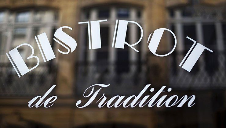 Sign reading “BISTROT de Tradition” in white script over a blurred storefront backdrop