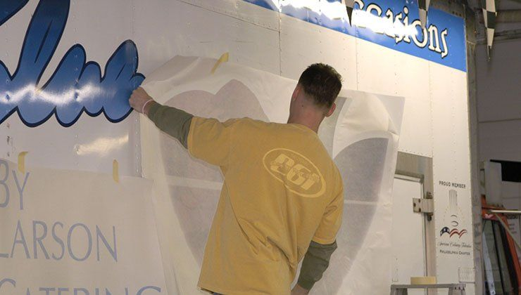 Man in yellow shirt applying a large white decal to a wall with blue graphics