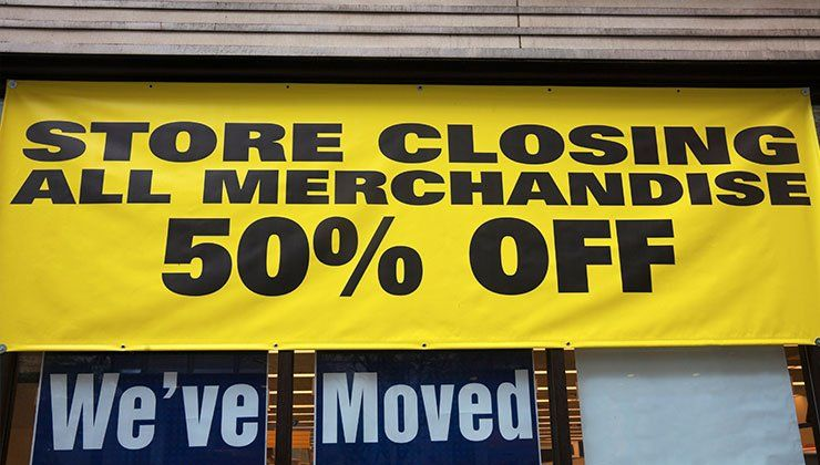 Store closing sign: all merchandise 50% off on yellow banner above storefront.