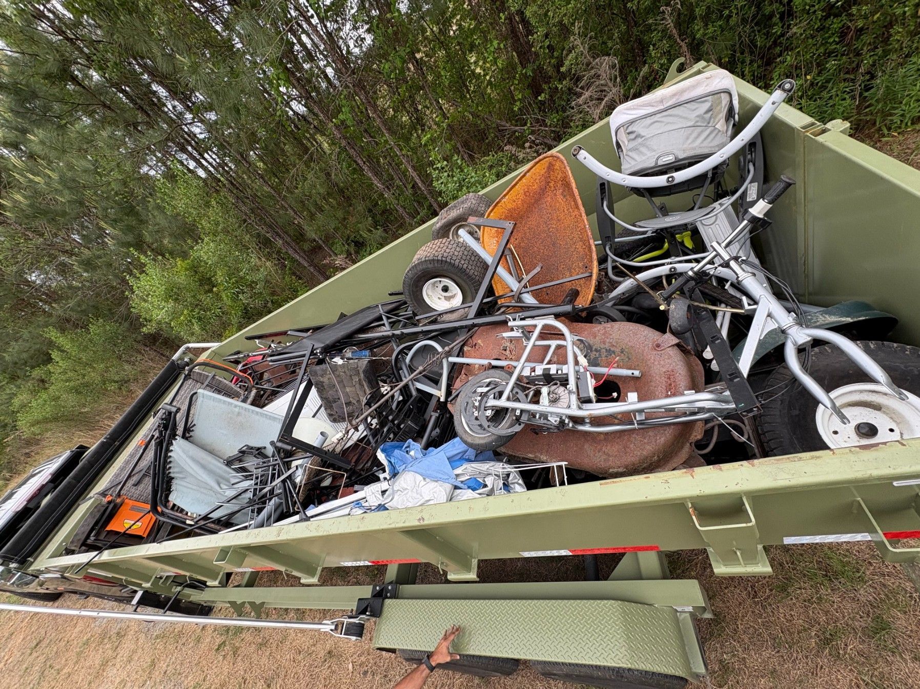 Overturned dumpster filled with broken bicycles and metal debris beside a wooded area