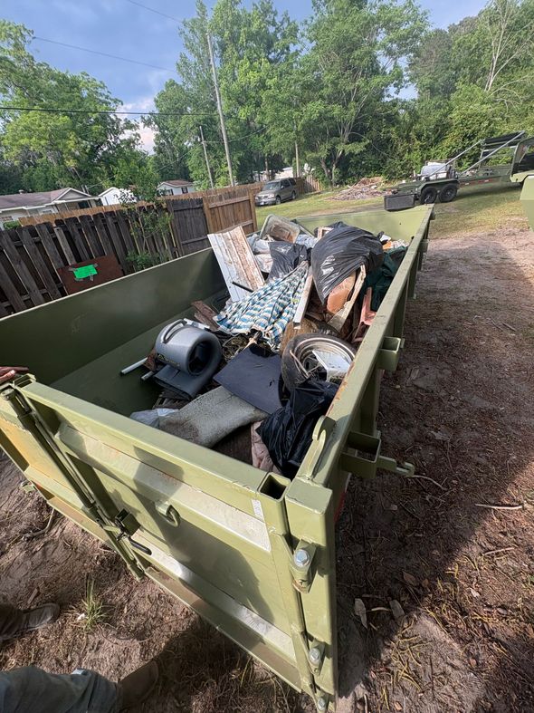 Green dumpster filled with scrap metal and debris in a yard outdoors
