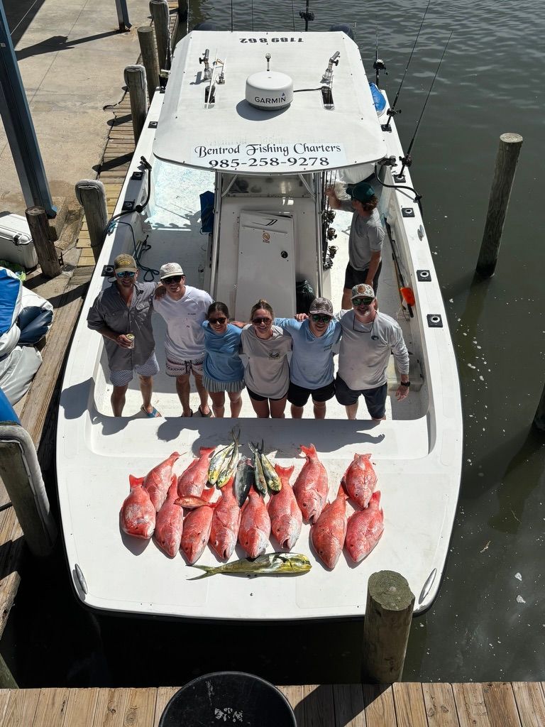 A group of people stand on a boat docked at a pier, with a large catch of red snapper arranged on the deck.
