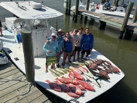 A group of people stands on a boat at a dock with a large catch of fish laid out on the deck.