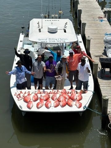 A group of people standing on a fishing boat at a dock, with a large catch of fish spread out on the deck.