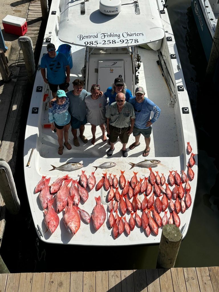A group of people standing on a boat deck with a large catch of red snapper and other fish spread out before them.