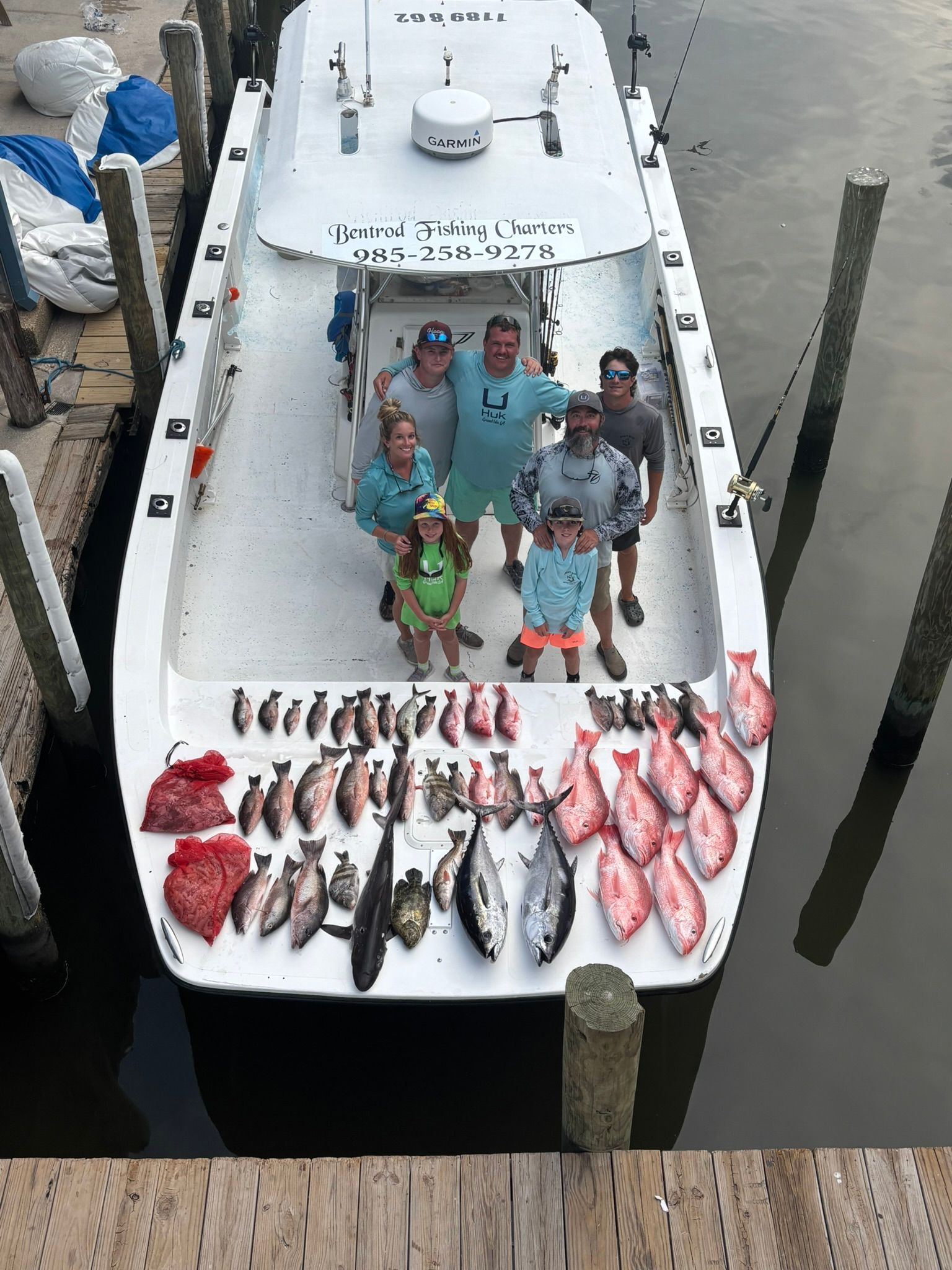 A group of people standing on a boat deck surrounded by their catch of fish, docked at a pier.