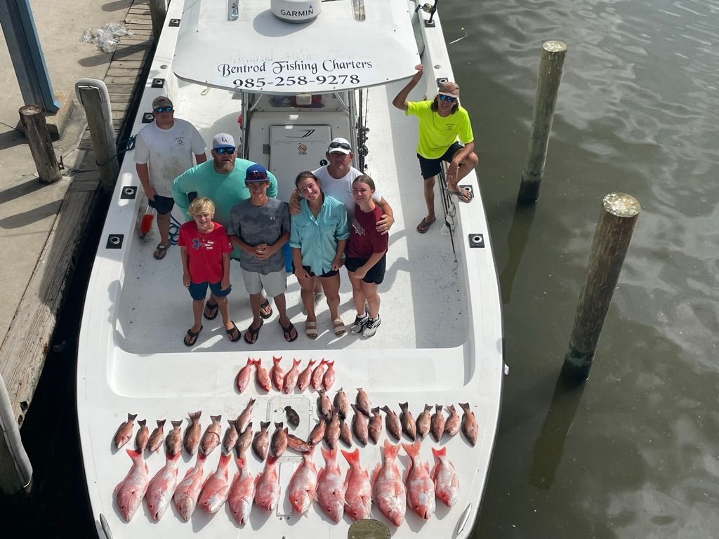 A group of people standing on a boat deck next to a large catch of fish, docked at a pier.