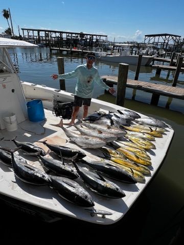 A person standing on a boat deck displaying a large catch of tuna and mahi-mahi fish at a marina.