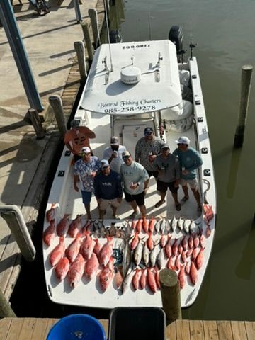 A group of people on a boat docked at a pier, standing behind a large catch of fish spread out on the deck.