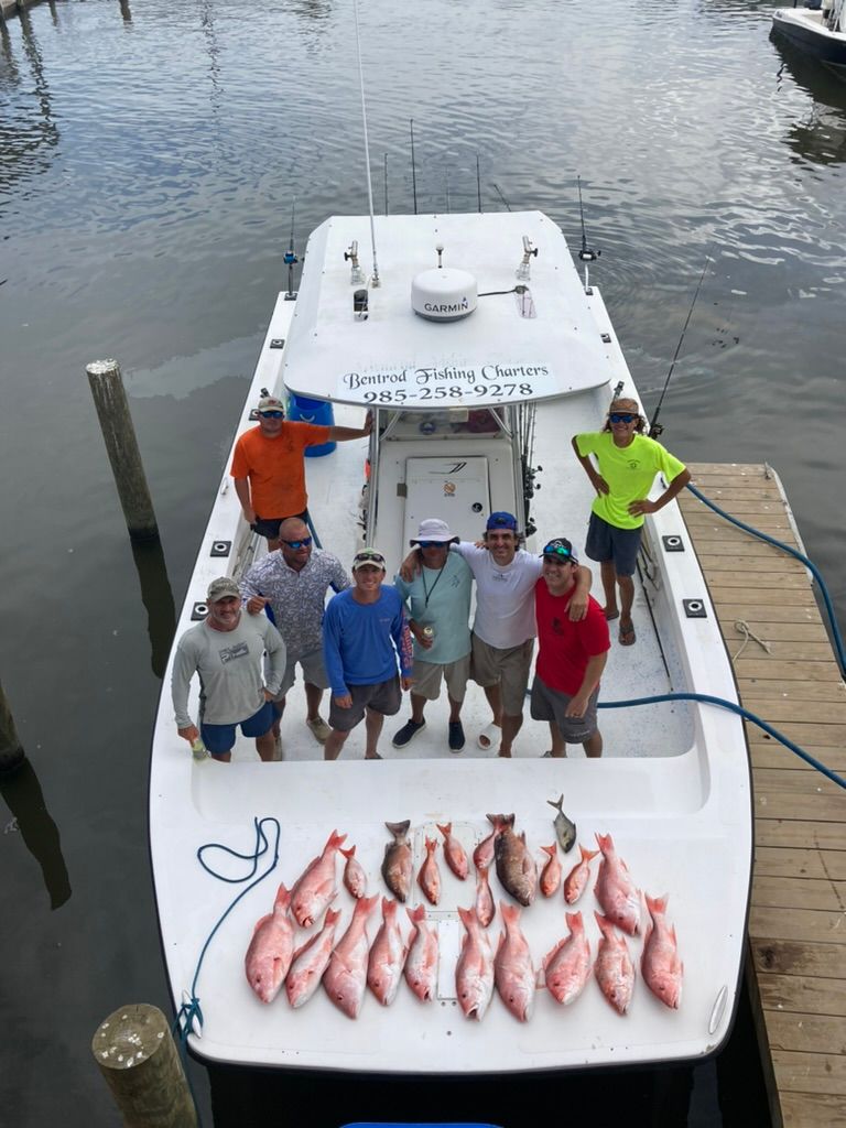 A group of people standing on a boat at a dock next to a large catch of fish spread out on the deck.