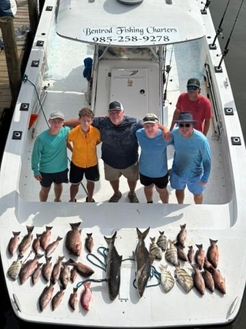 Six people stand on a charter fishing boat, posing with a large catch of various fish spread across the deck.