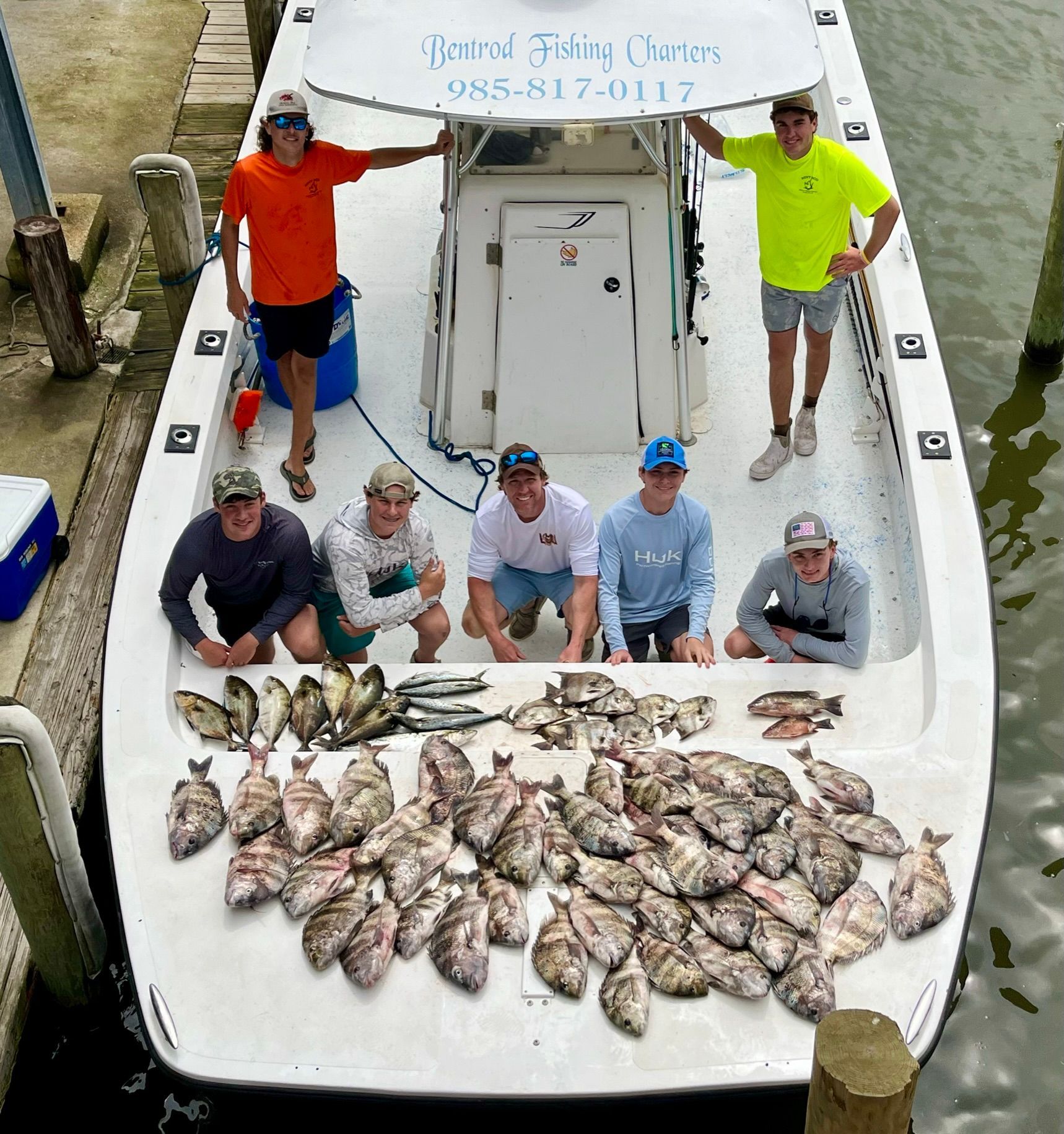 A group of people stand on a boat with a large catch of fish spread out on the deck.