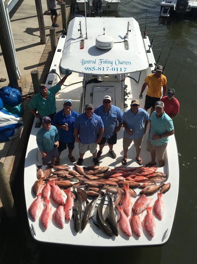 A group of people standing on a boat deck filled with a large catch of fish, docked at a pier.