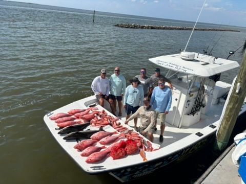 A group of people standing on a boat deck alongside a large haul of freshly caught red snapper and other fish.