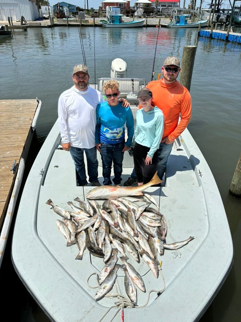 Four people stand on a boat at a marina with a large catch of fish spread across the deck.