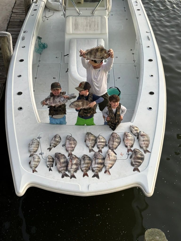 Four people on a white boat hold fish, with many more catch fish arranged on the deck in front of them.