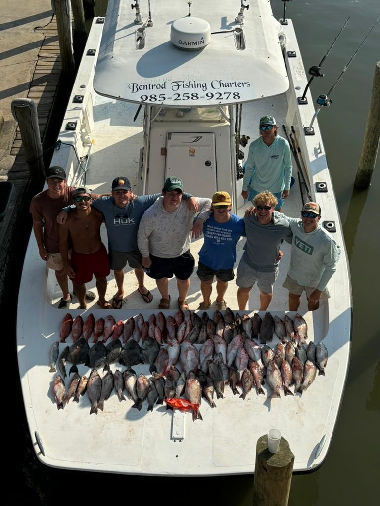 A group of people stands on a boat deck behind a large collection of freshly caught fish at a dock.
