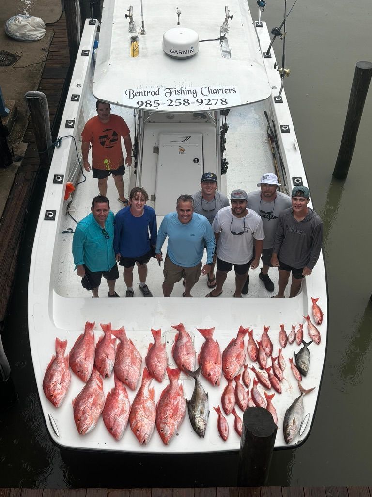 A group of people stand on a boat with a large catch of red snapper and other fish spread out on the deck.