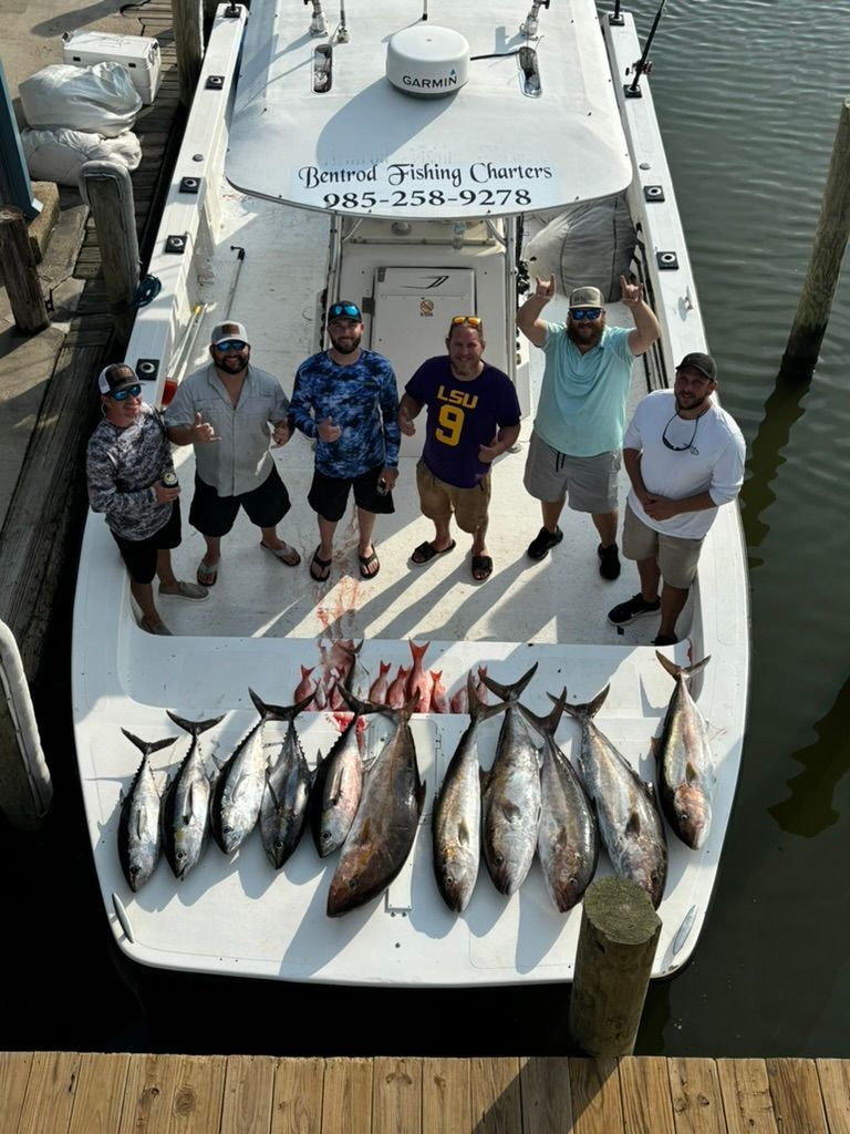 A group of people standing on a boat deck with their day's catch of fish arranged in front of them at a dock.