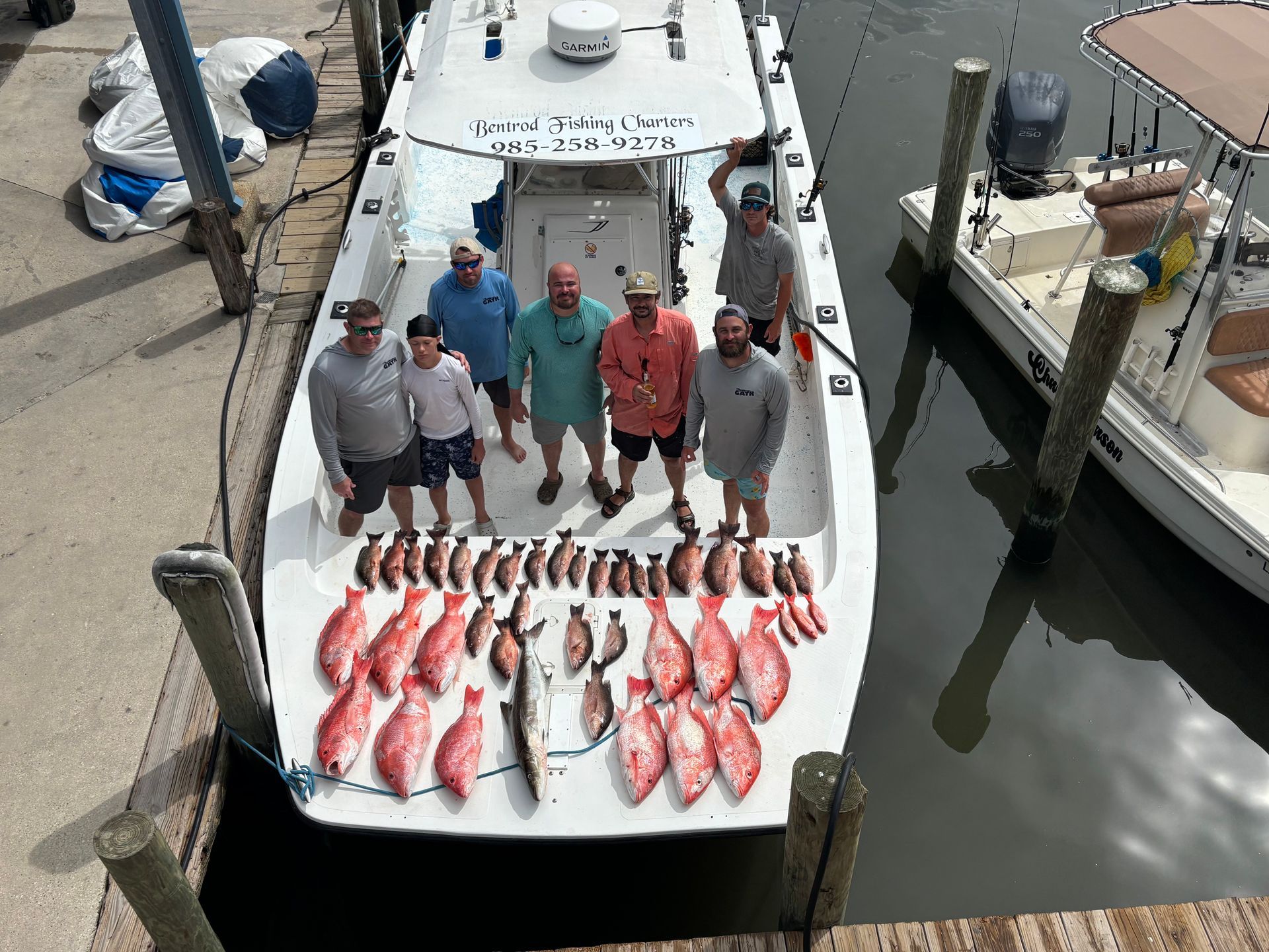 A group of people standing on a boat with their catch of red snapper fish arranged on the deck at a marina.