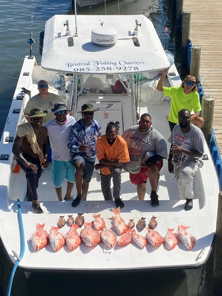 A group of people standing on a boat deck behind a large catch of fish, parked at a wooden dock.