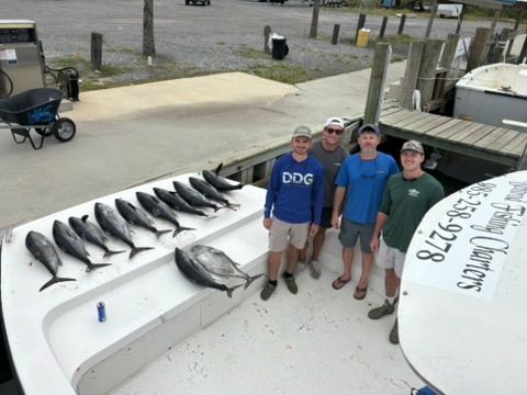 Four people stand on a boat deck next to a row of tuna caught during a fishing charter.