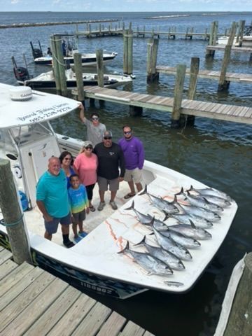 A group of people standing on a boat docked at a marina, with their catch of several fish laid out on the deck.