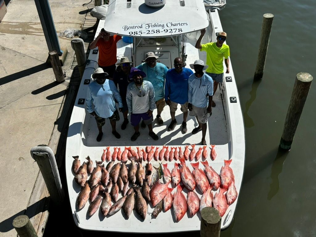 A group of people standing on a boat docked at a pier, surrounding a large collection of fresh fish caught on the deck.