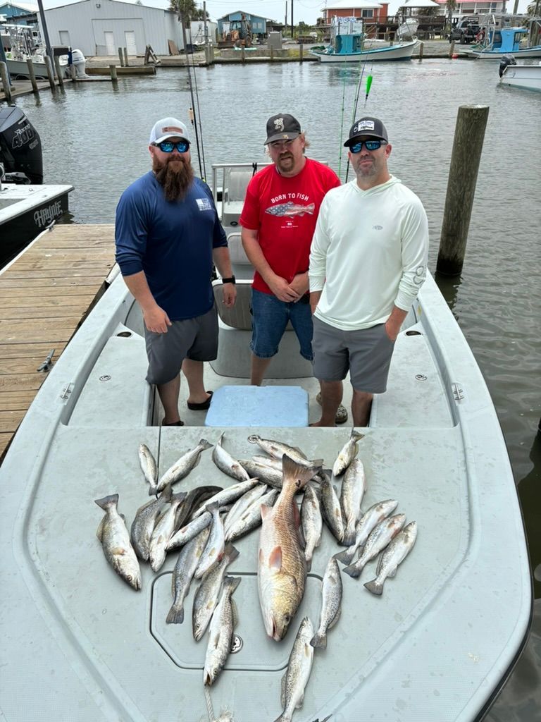 Three people wearing hats and sunglasses stand on a boat deck behind a large catch of fish.