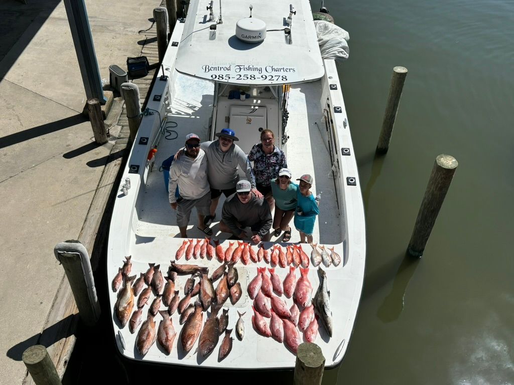 A group of people stand on a boat docked at a pier, surrounding a large catch of fish laid out on the deck.