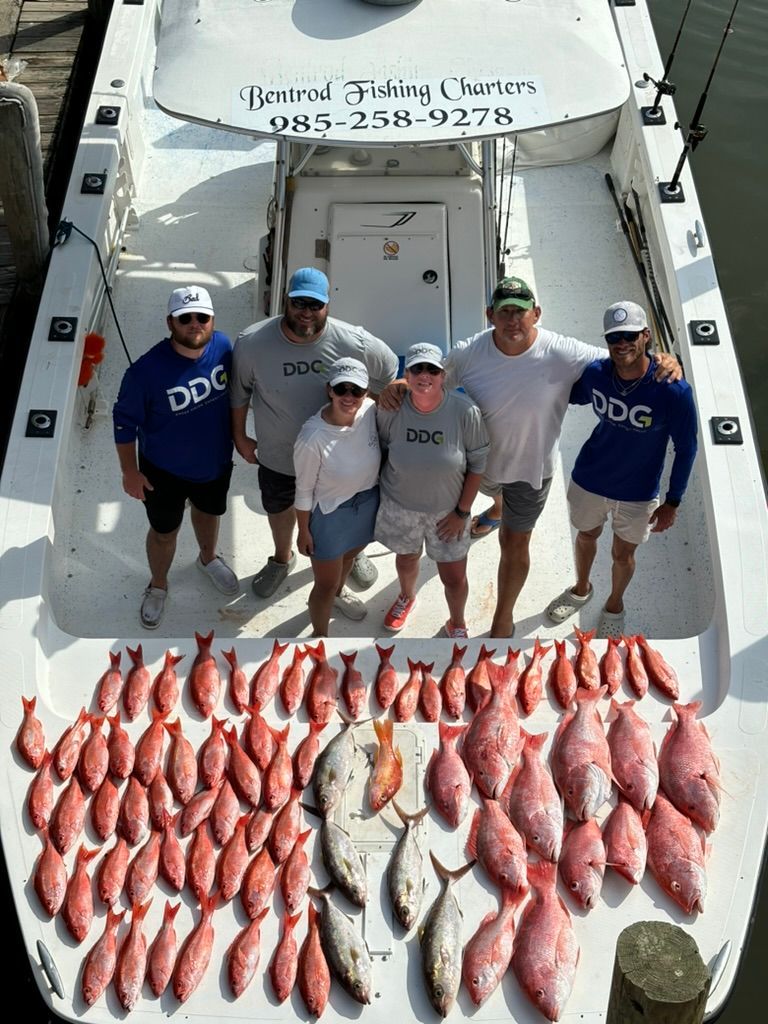 Six people pose on a boat deck behind a large catch of red snapper and several silver fish.