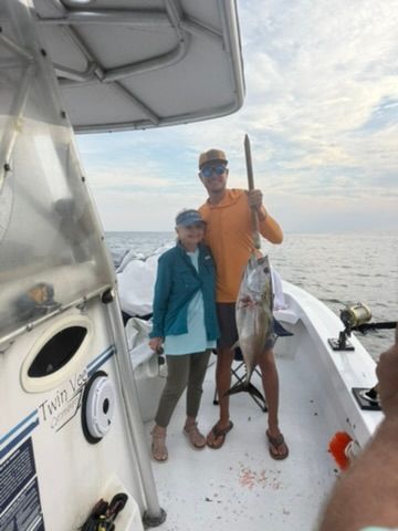 Two people standing on a boat holding a caught fish, with the ocean in the background.