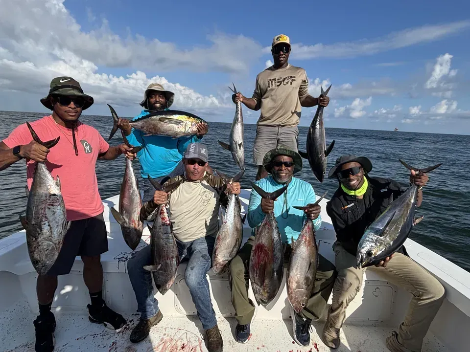 Six people on a boat holding fresh catches of tuna on a sunny day at sea.