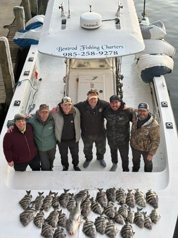 Six people stand on a boat deck behind a large catch of striped fish, with a charter boat sign in the background.