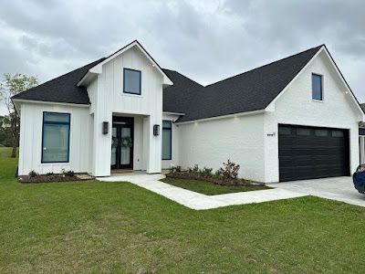 A white house with a black roof and a black garage door.