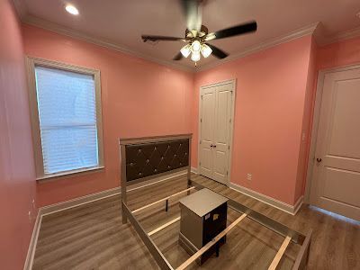 A bedroom with pink walls , a bed and a ceiling fan.