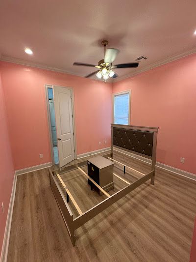 A bedroom with pink walls and a bed and a ceiling fan.