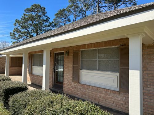 A brick house with a porch and trees in the background.