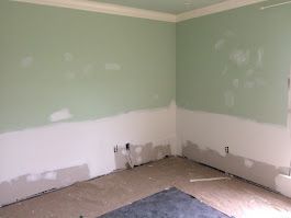 A room with green walls and white trim is being painted.