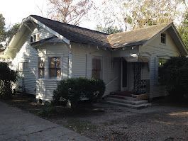 A small white house with a gray roof and a driveway in front of it.