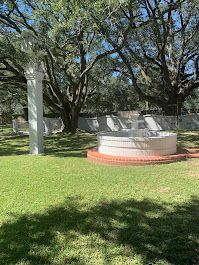 A fountain in the middle of a lush green field with trees in the background.
