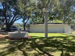 There is a fountain in the middle of the grass in front of a house.