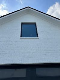 A white brick house with a window on the roof.