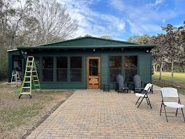 A green house with a screened in porch and chairs in front of it.
