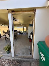 A green trash can is sitting next to a door in a house.