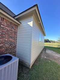 The side of a house with a brick wall and a white siding and an air conditioner.