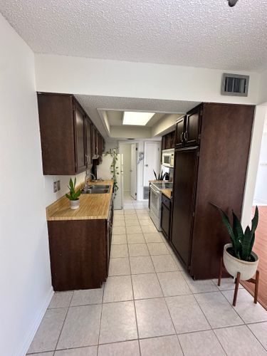 A kitchen with brown cabinets , a stove , a refrigerator , a sink , and a potted plant.