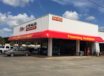 A white building with a red awning and cars parked in front of it.