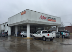 A white truck is parked in front of a car dealership.