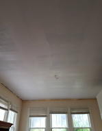 A living room with a white ceiling and three windows.